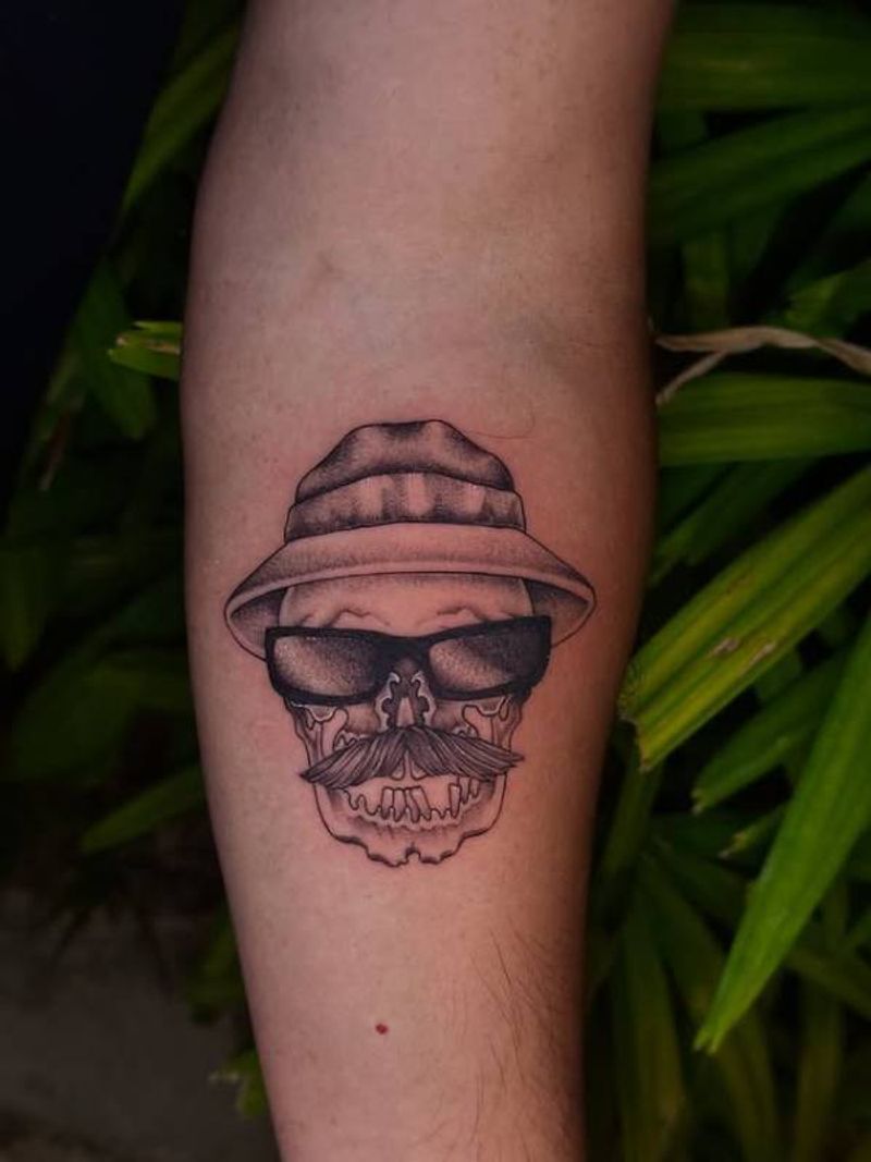 Black and grey illustrative skull with hat and sunglasses tattoo on forearm