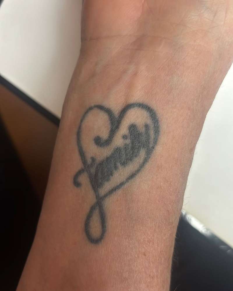 Black and grey script 'family' tattoo with heart on forearm.