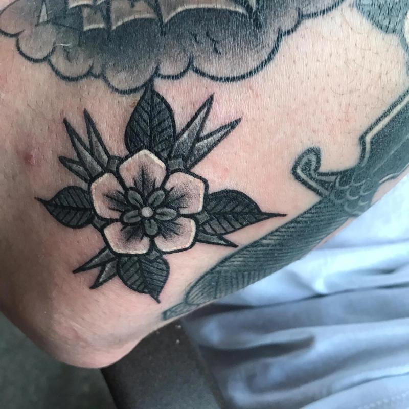 Black and grey traditional flower tattoo on upper arm