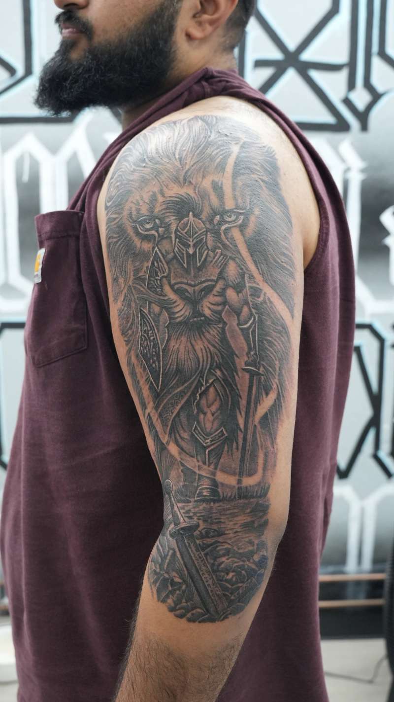 Black and grey illustrative knight and lion tattoo on upper arm