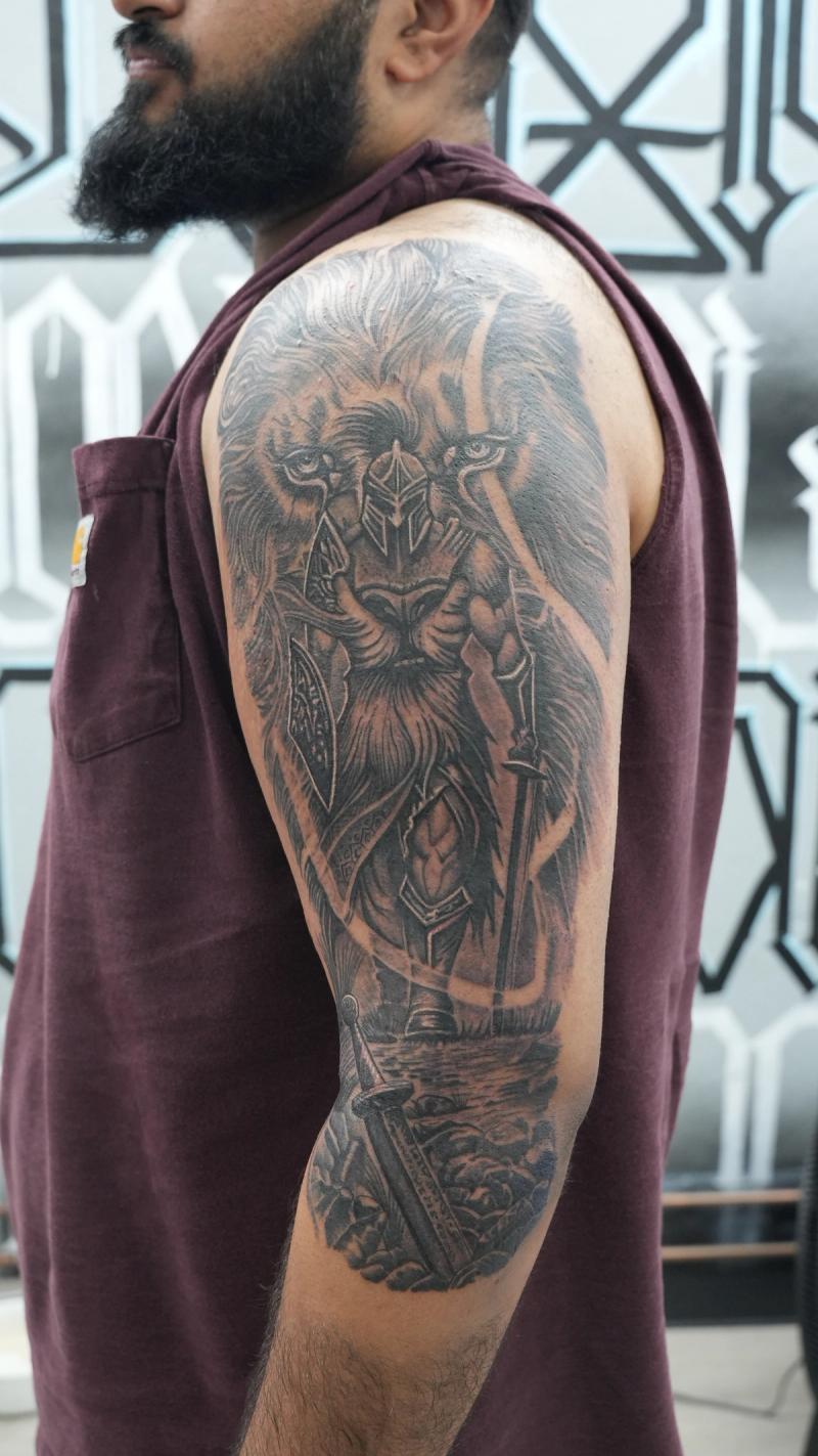 Black and grey illustrative knight and lion tattoo on upper arm