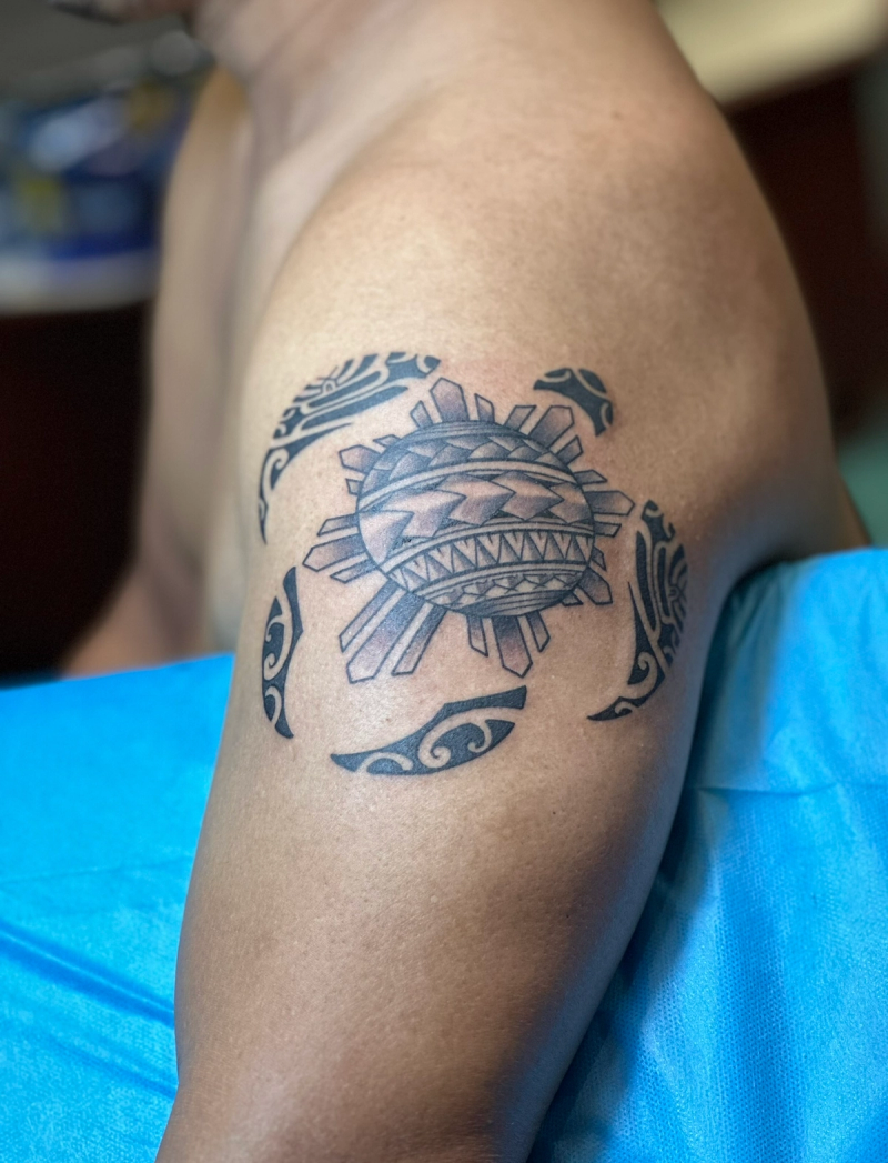 Black and grey tribal sun tattoo on upper arm