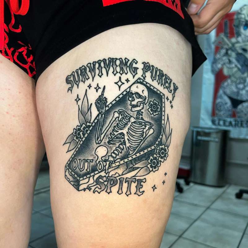 skeletal coffin and lettering tattoo on thigh