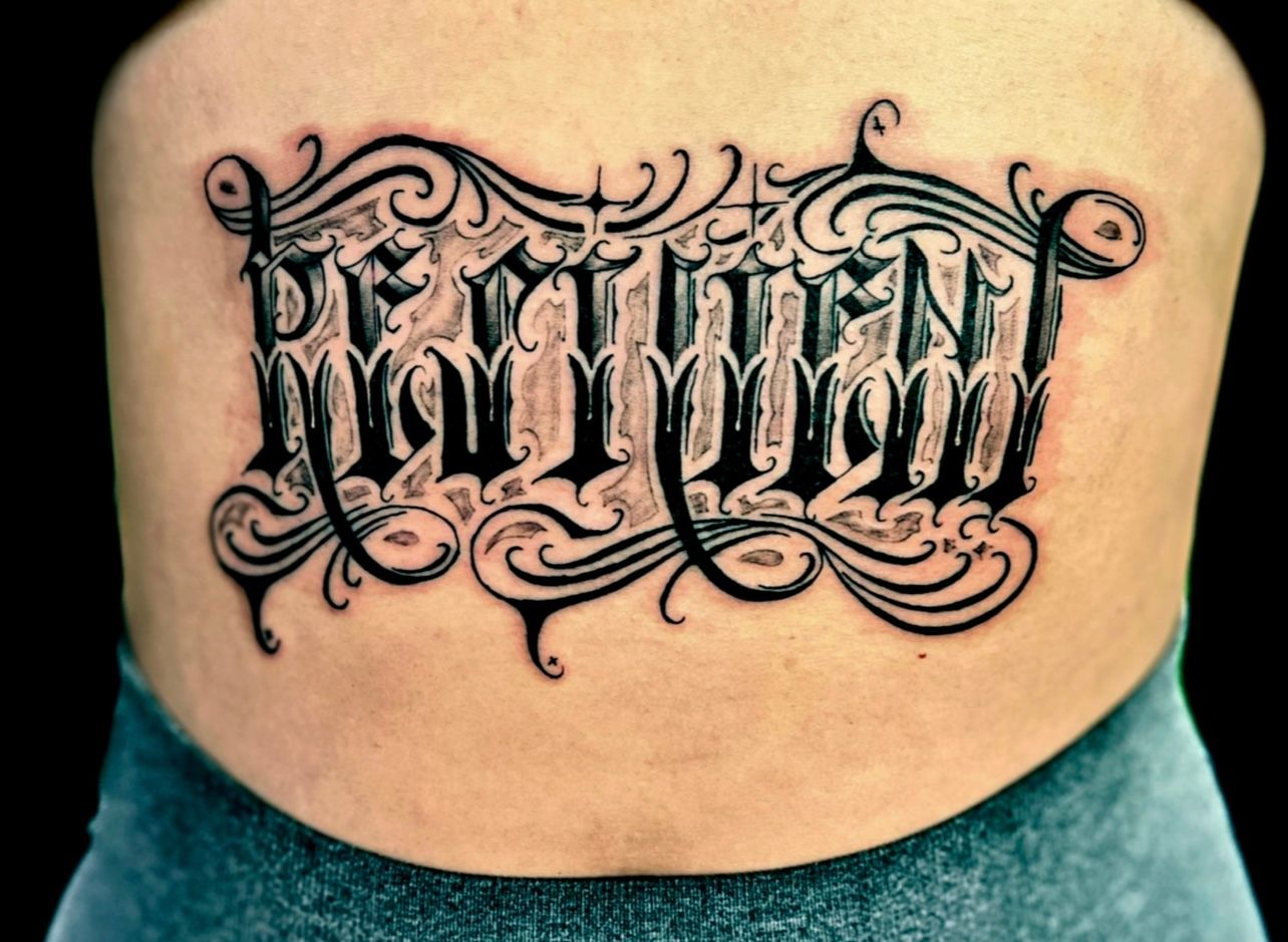 Black and grey gothic script tattoo on lower back