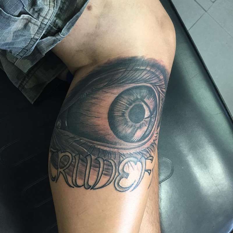 Black and grey realistic eye with script lettering on thigh