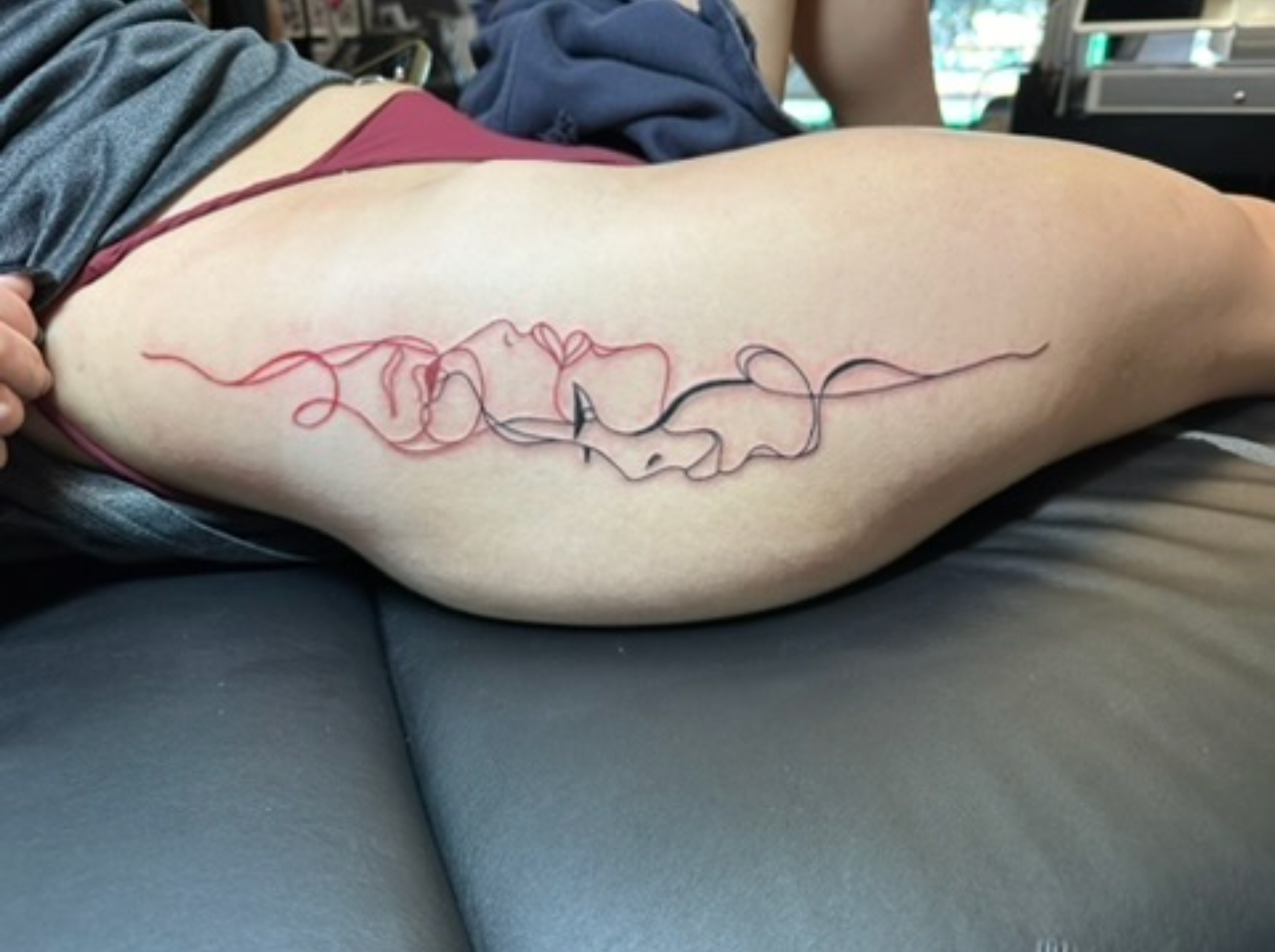 Red and black minimalist continuous line faces tattoo on thigh