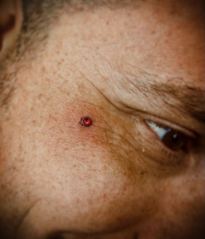 Small red circle piercing on face near the eye
