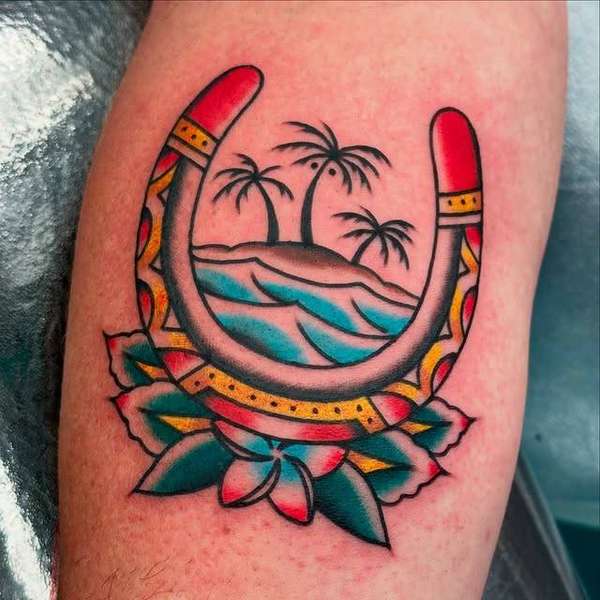 Vibrant color tattoo of a horseshoe with tropical island scene on upper arm