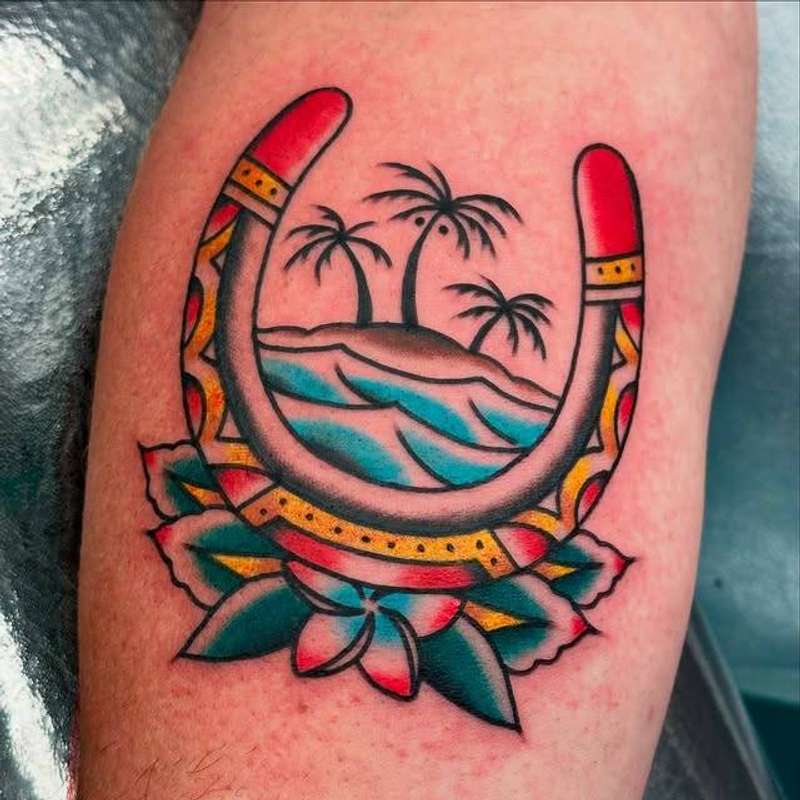 Vibrant color tattoo of a horseshoe with tropical island scene on upper arm
