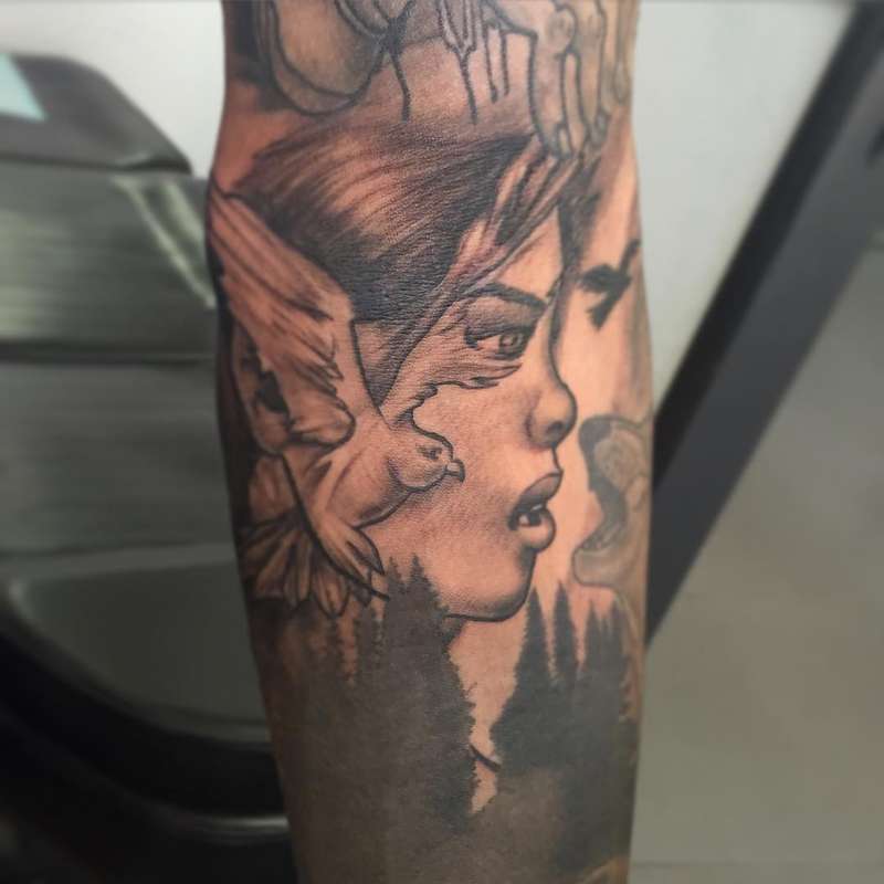 Black and grey illustrative tattoo of a woman's face and bird on the forearm