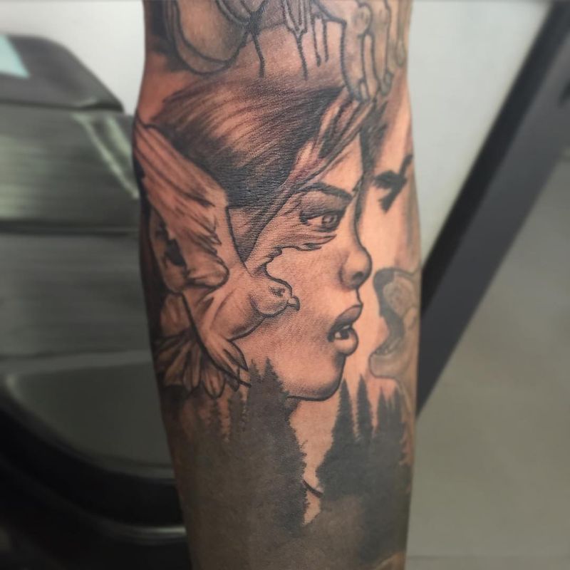 Black and grey illustrative tattoo of a woman's face and bird on the forearm