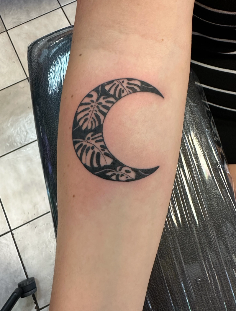 Solid black crescent moon with botanical design on forearm