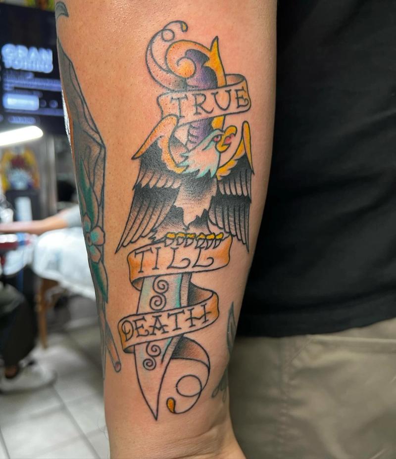 Colorful traditional eagle and dagger tattoo with script on forearm