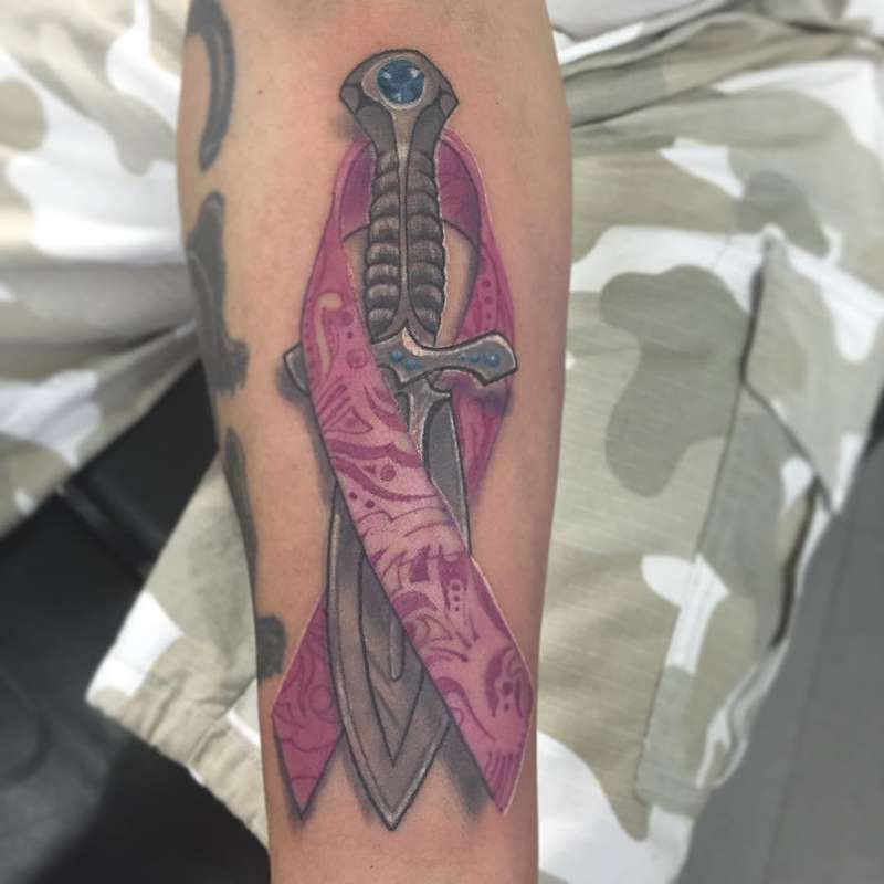 tattoo of a sword with a ribbon on a forearm
