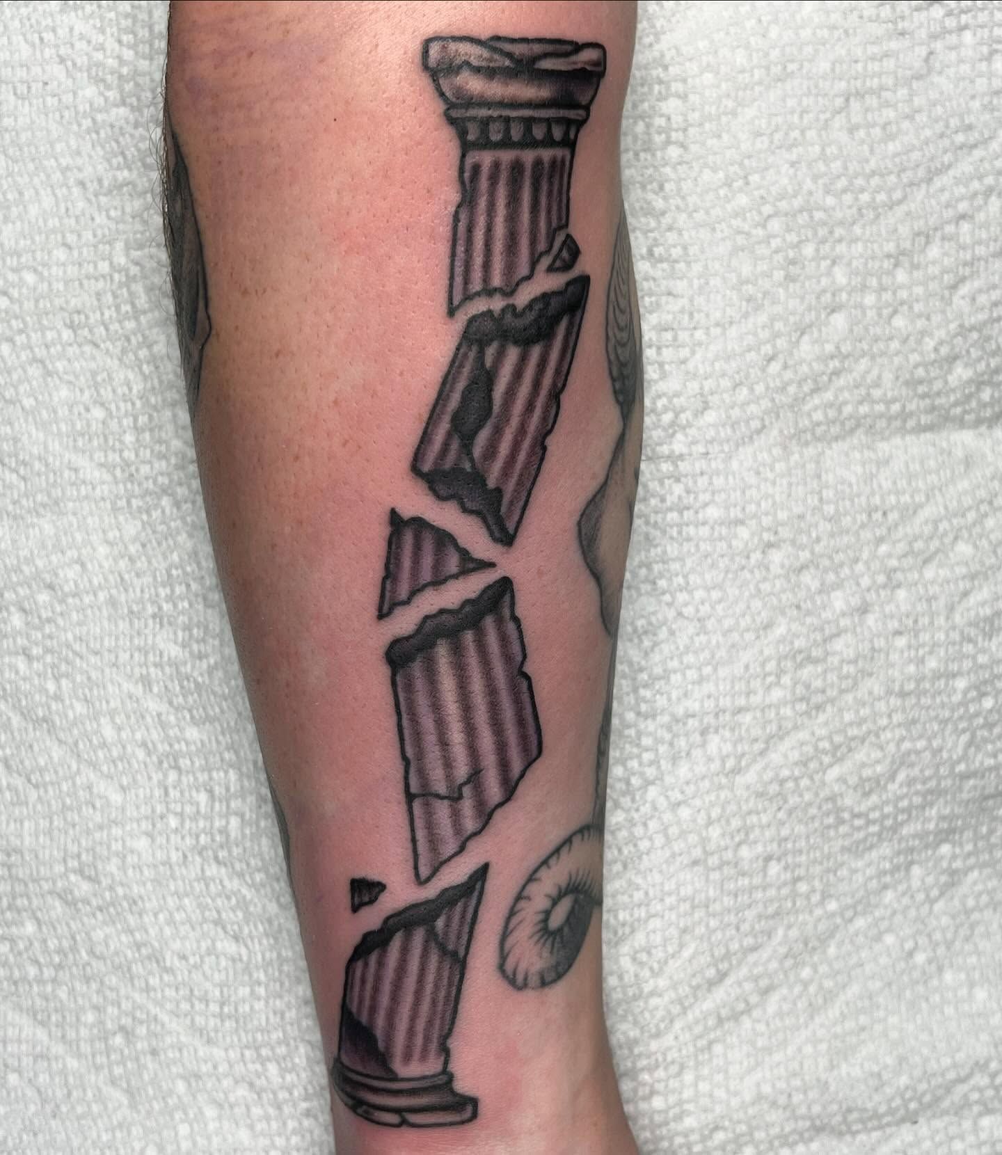 Black and grey illustrative broken column tattoo on forearm.