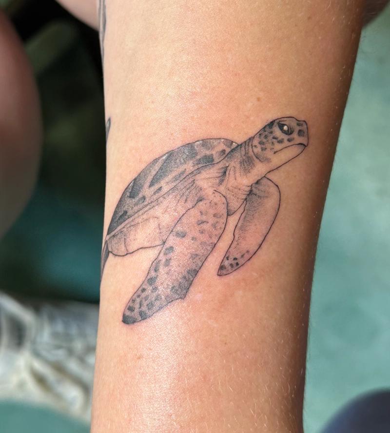 Black and grey illustrative sea turtle tattoo on forearm