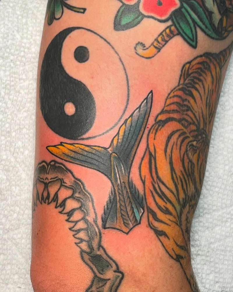 Yin yang, whale tail, and floral tattoo on upper arm with blackwork and color