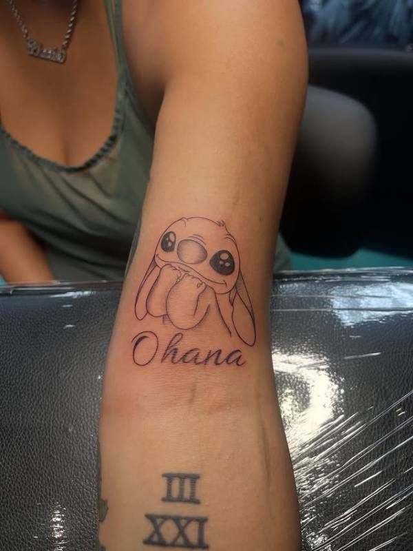 Black and grey illustrative cartoon and script tattoo on forearm