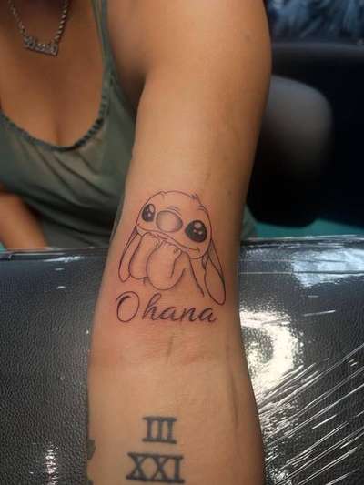 Black and grey illustrative cartoon and script tattoo on forearm