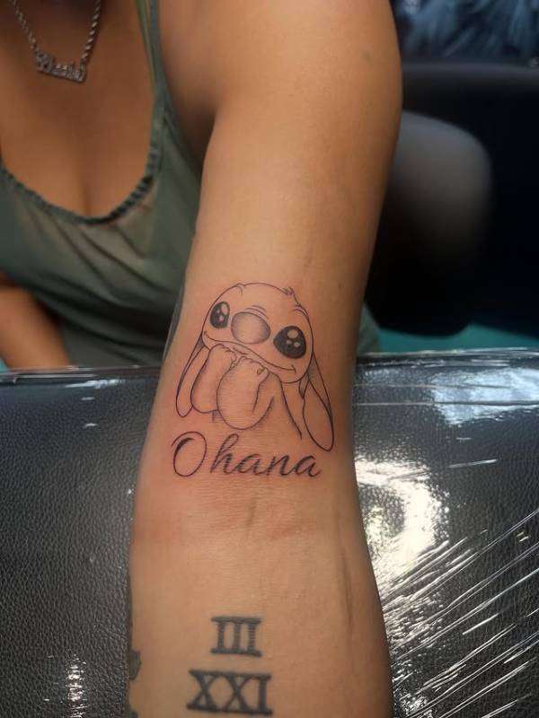 Black and grey illustrative cartoon and script tattoo on forearm