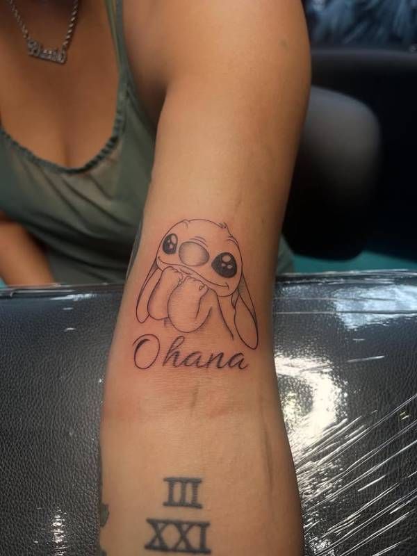 Black and grey illustrative cartoon and script tattoo on forearm