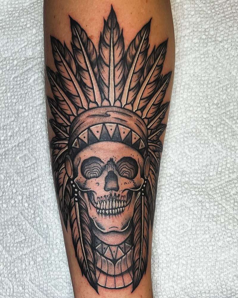Black and grey skull with feather headdress tattoo on forearm