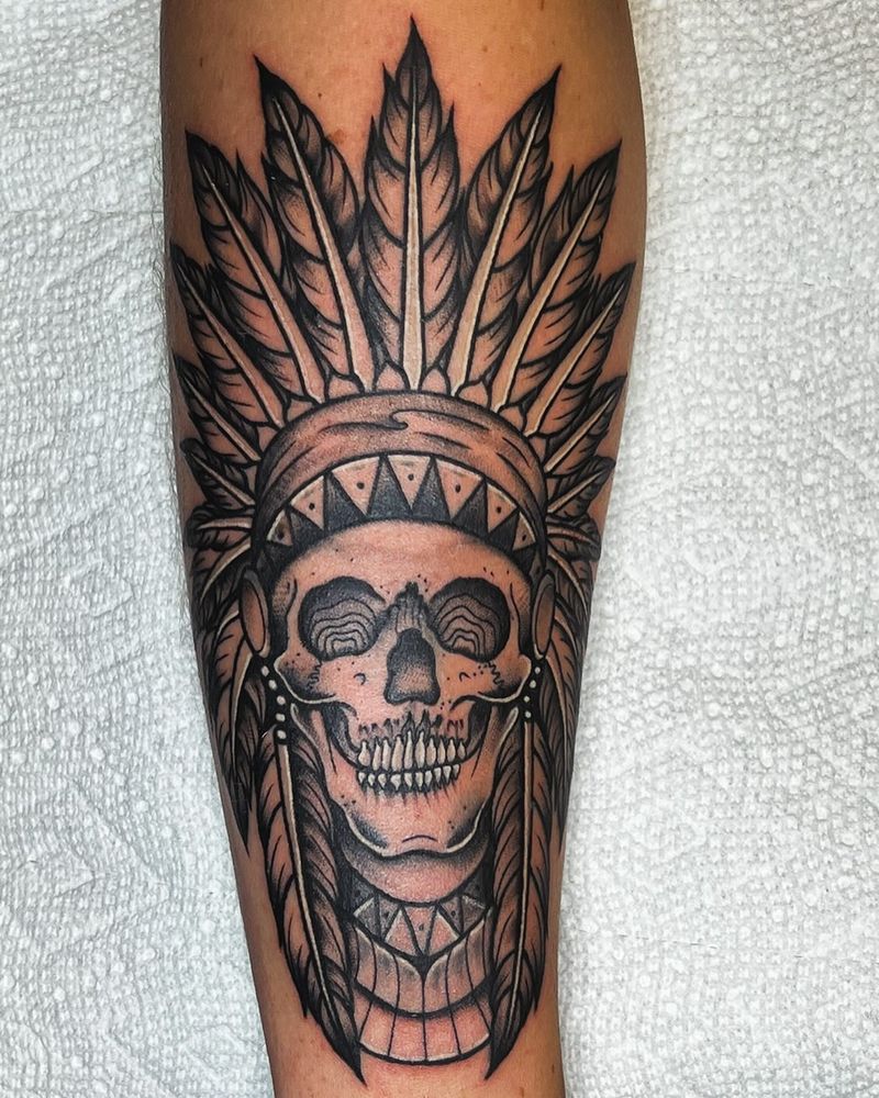 Black and grey skull with feather headdress tattoo on forearm