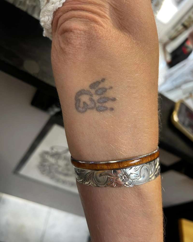 Black and grey minimalist paw print tattoo on forearm