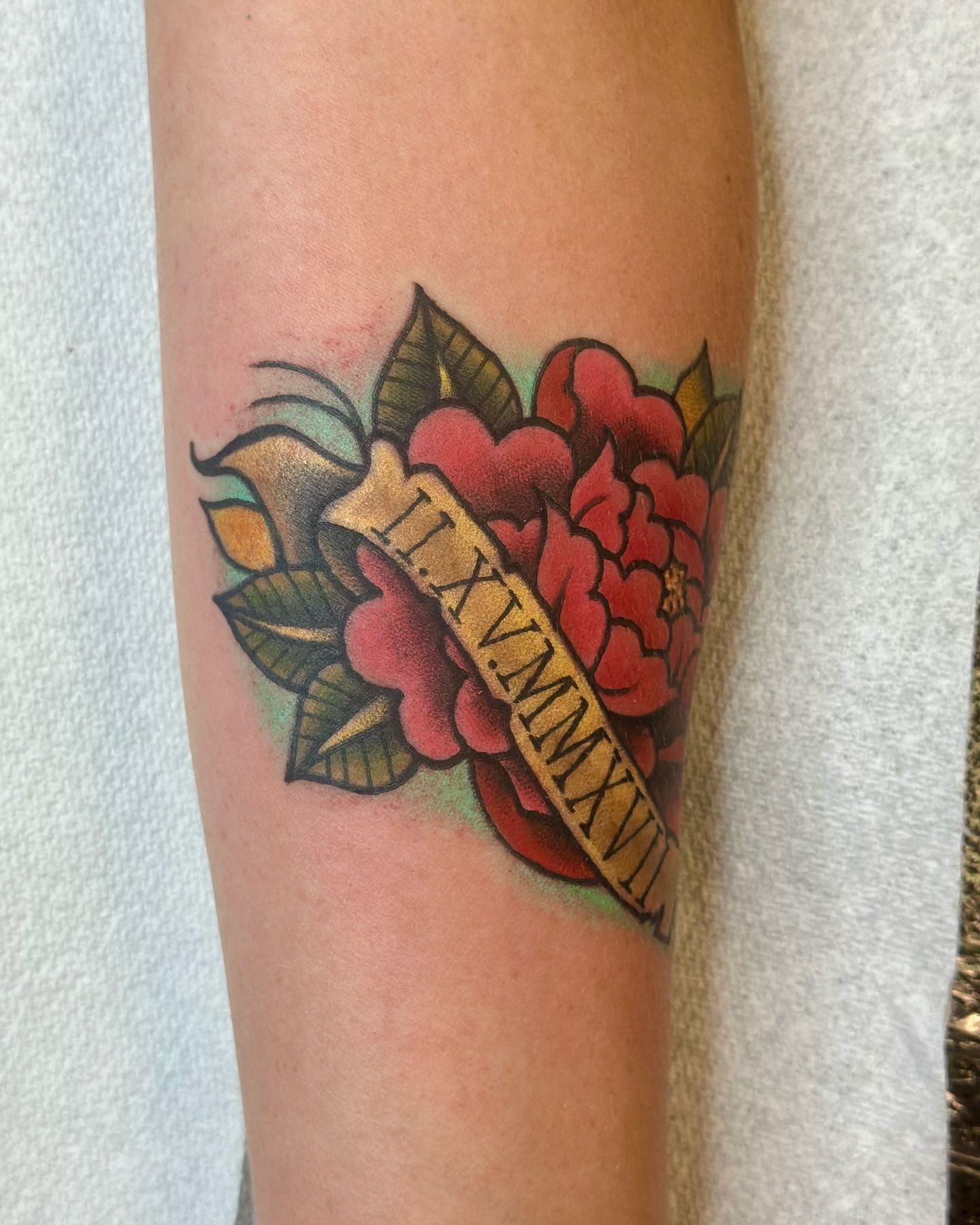 Colorful traditional rose tattoo with Roman numeral banner on forearm