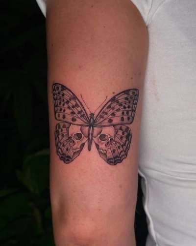 Black and grey illustrative butterfly with skulls on upper arm