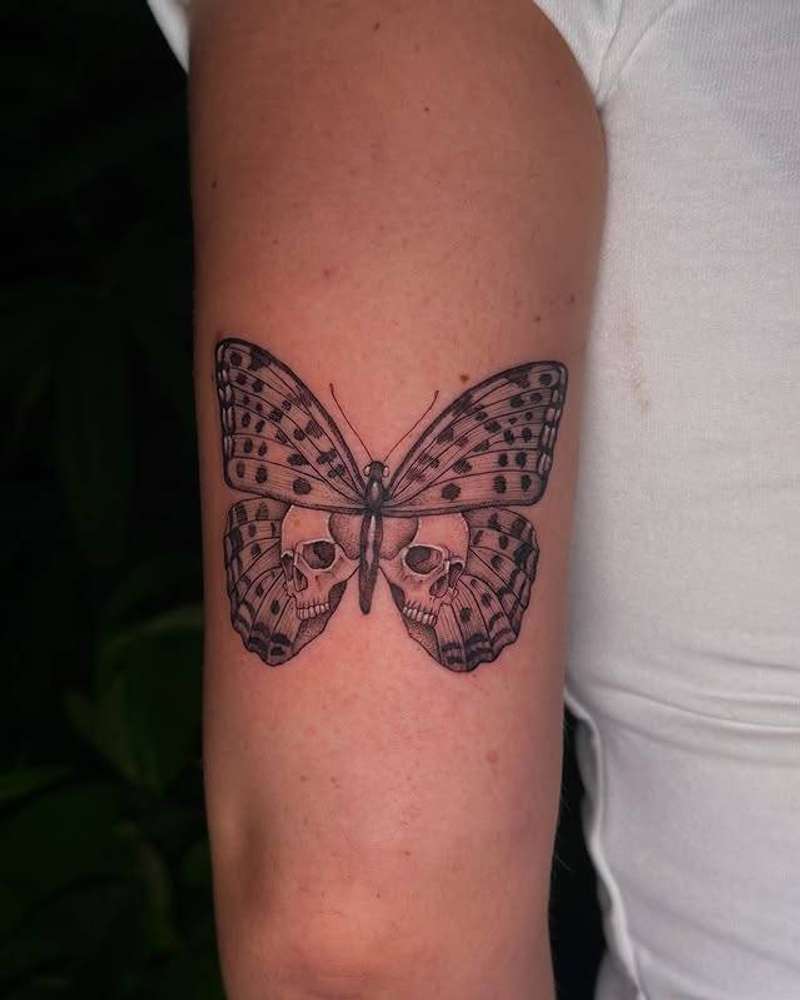Black and grey illustrative butterfly with skulls on upper arm