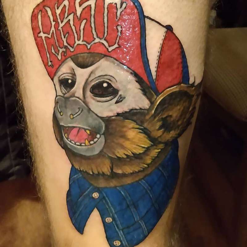 illustrative monkey tattoo with a hat and lettering on a thigh