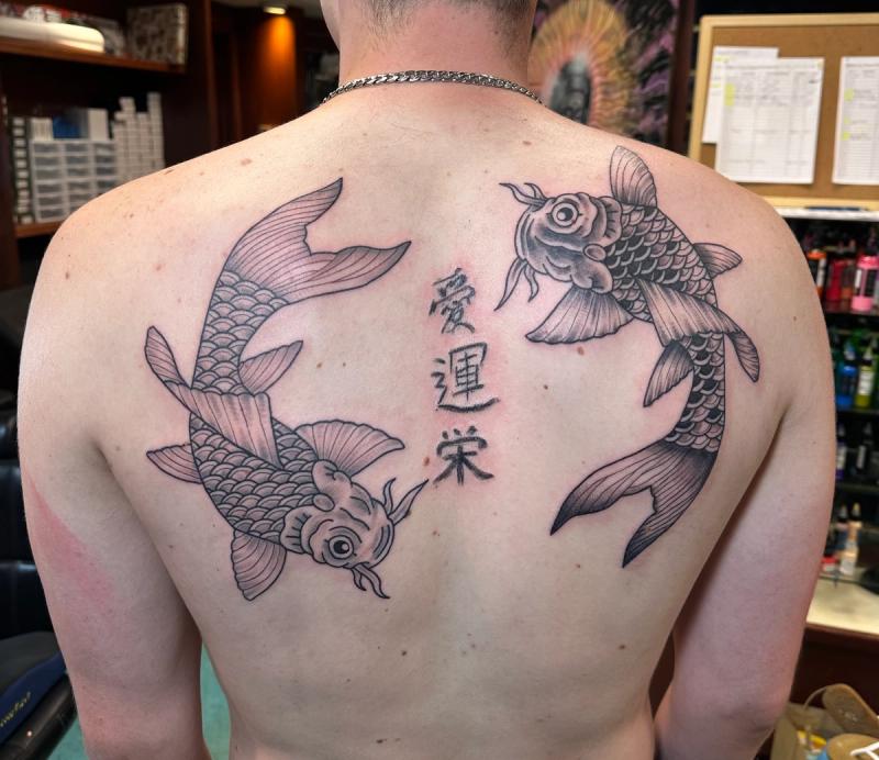 Black and grey koi fish tattoo with Japanese characters on upper back