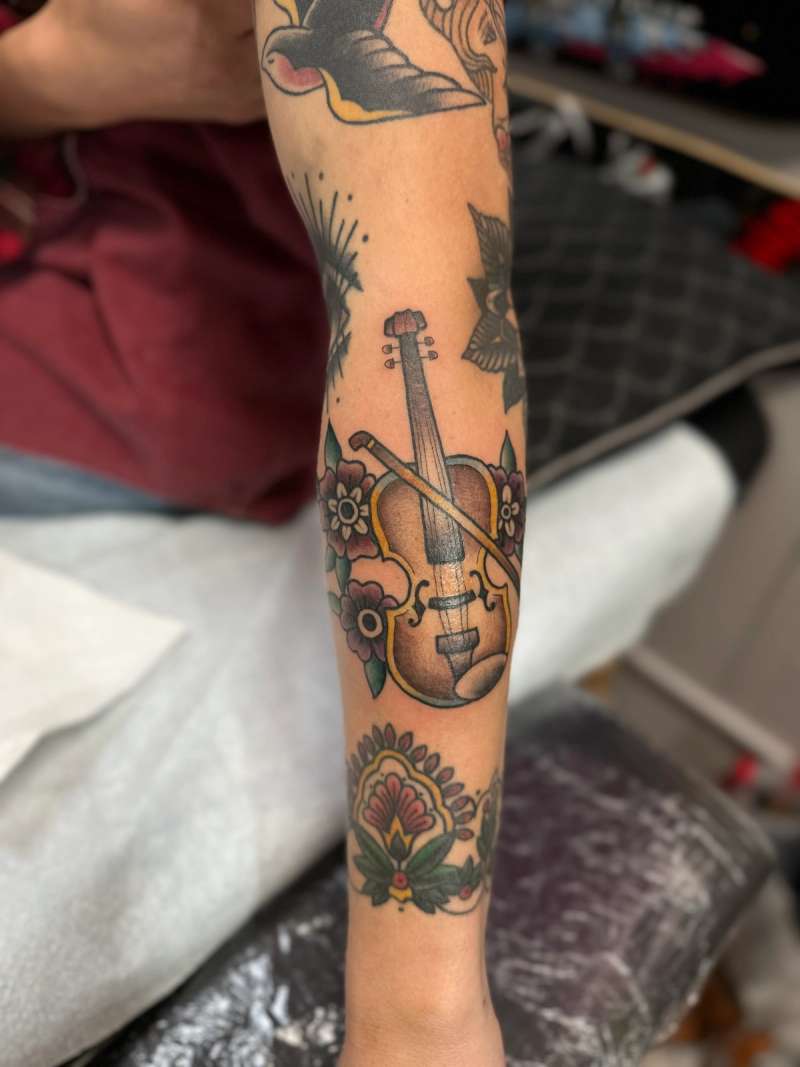 Colorful traditional tattoo of a violin surrounded by flowers on forearm