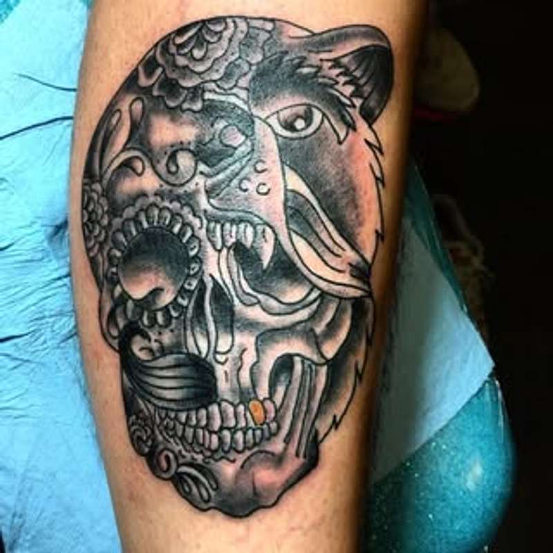 Black and grey illustrative bear and skull tattoo on forearm