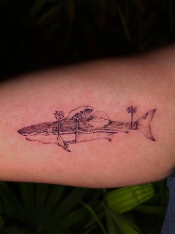 Black and grey illustrative shark with palm trees tattoo on forearm