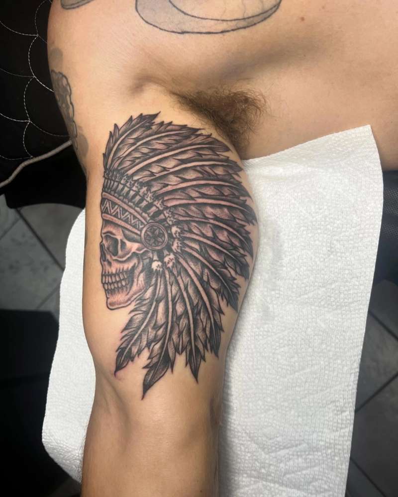 Black and grey illustrative skull with headdress on upper arm