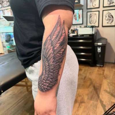 Black and grey wing tattoo on forearm