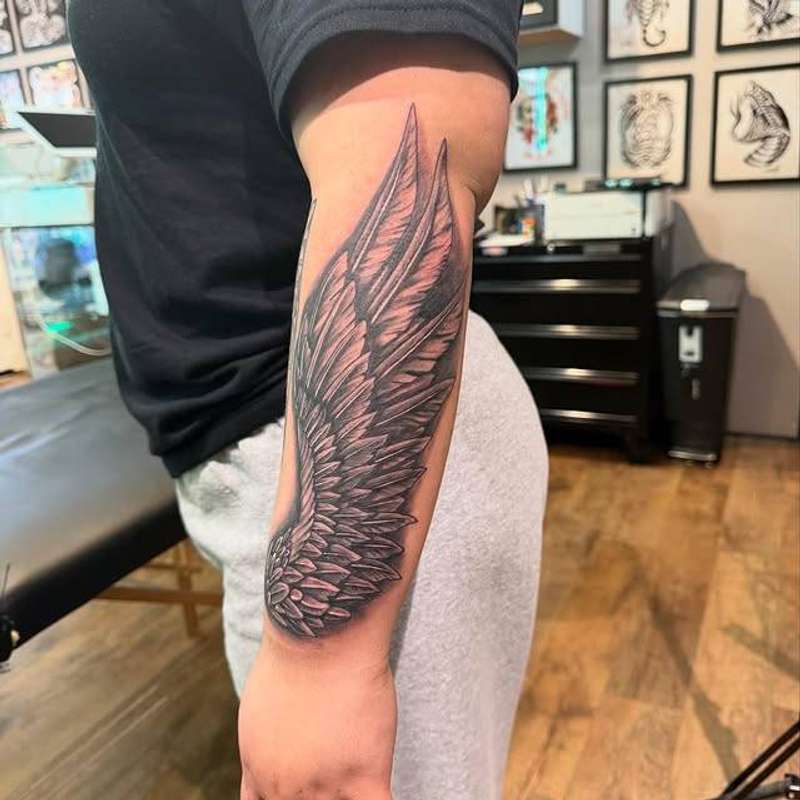 Black and grey wing tattoo on forearm