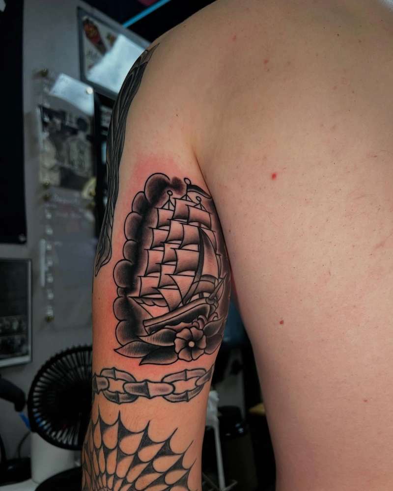 Black and grey traditional ship tattoo on upper arm