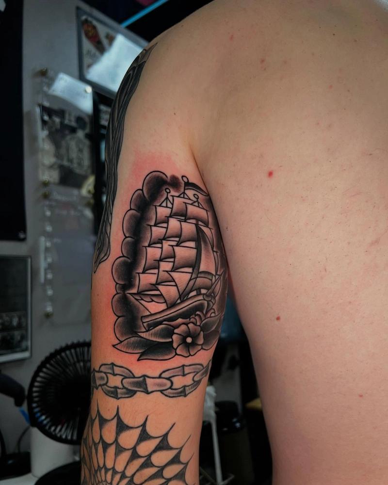 Black and grey traditional ship tattoo on upper arm