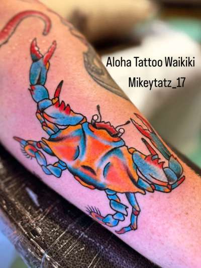 colorful traditional style crab tattoo on forearm with blue and orange coloring