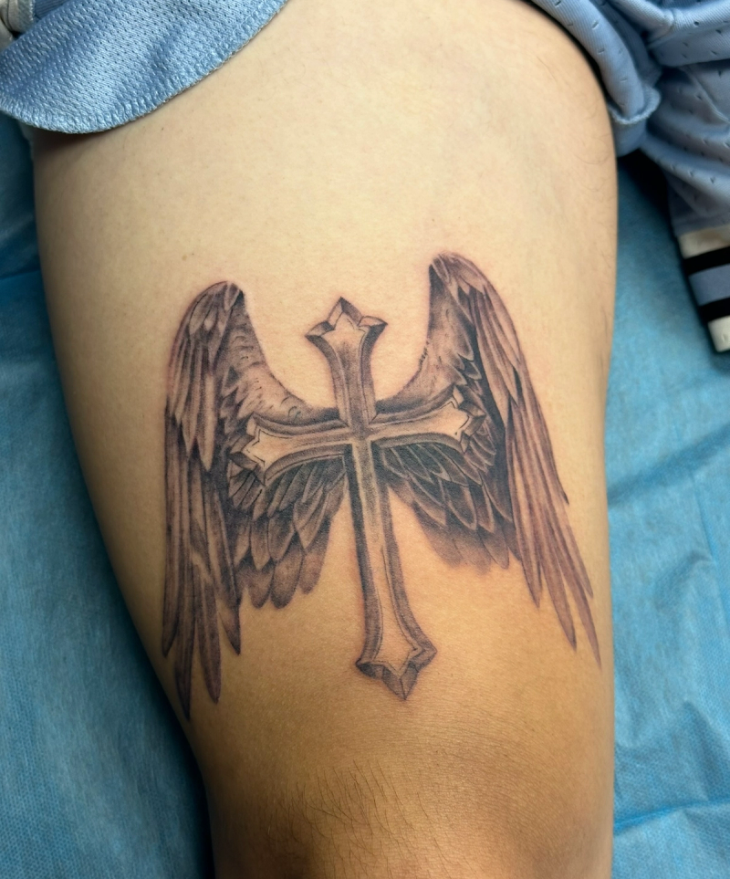 Black and grey winged cross tattoo on thigh