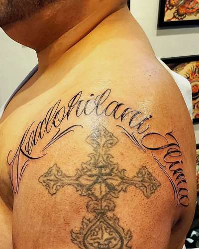 Black and grey script and cross tattoo on shoulder