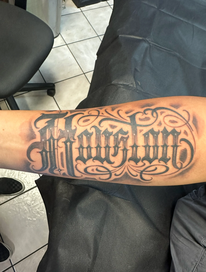Black and grey stylized lettering tattoo on forearm