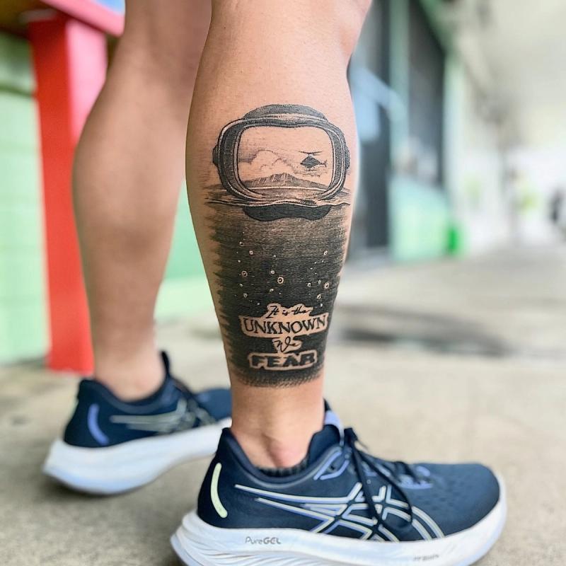 astronaut helmet tattoo with lettering on calf