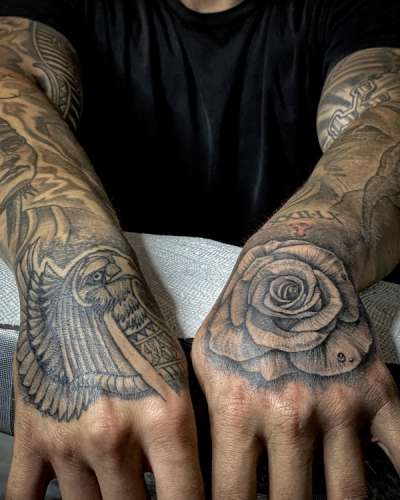 Black and grey rose tattoo on right hand and bird tattoo on left hand.