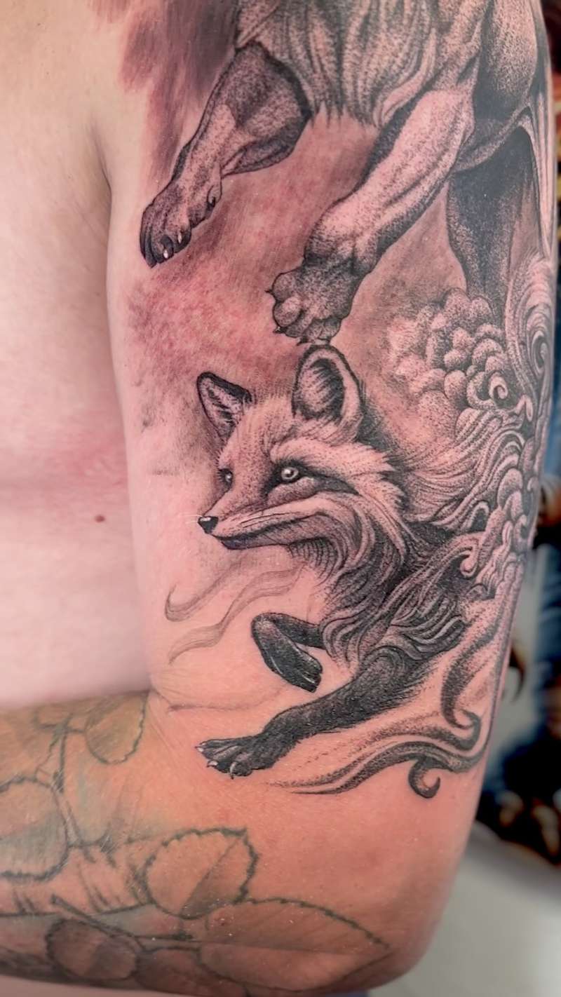 Black and grey illustrative fox with clouds tattoo on upper arm