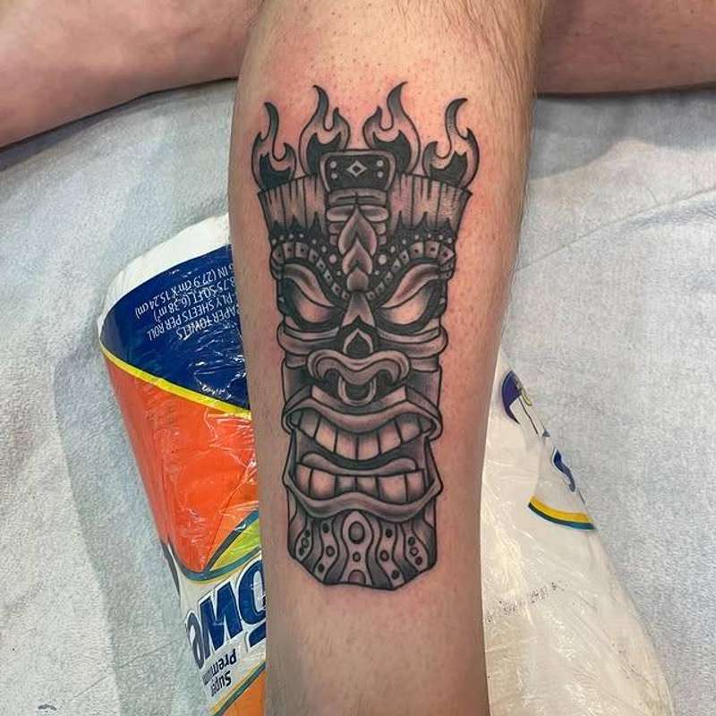 Black and grey tribal mask tattoo on calf