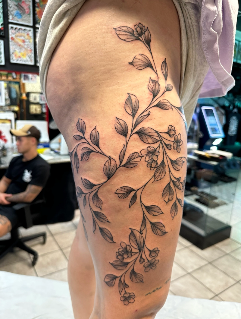 Black and grey floral vine tattoo on thigh